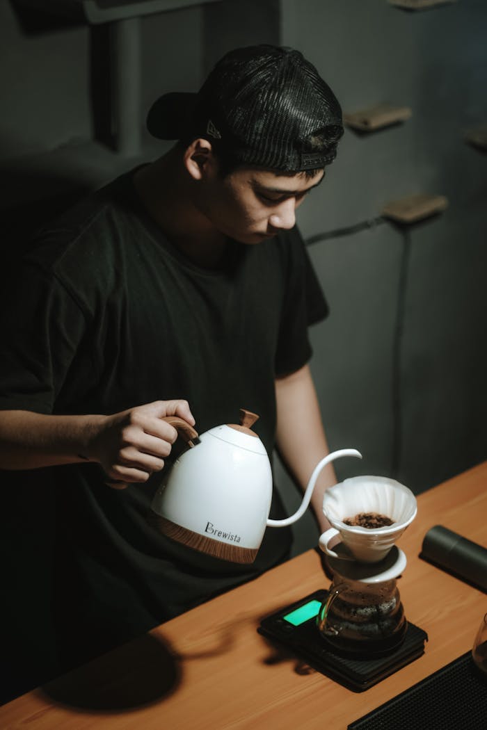 A barista skillfully pours hot water over coffee grounds in a dripper.