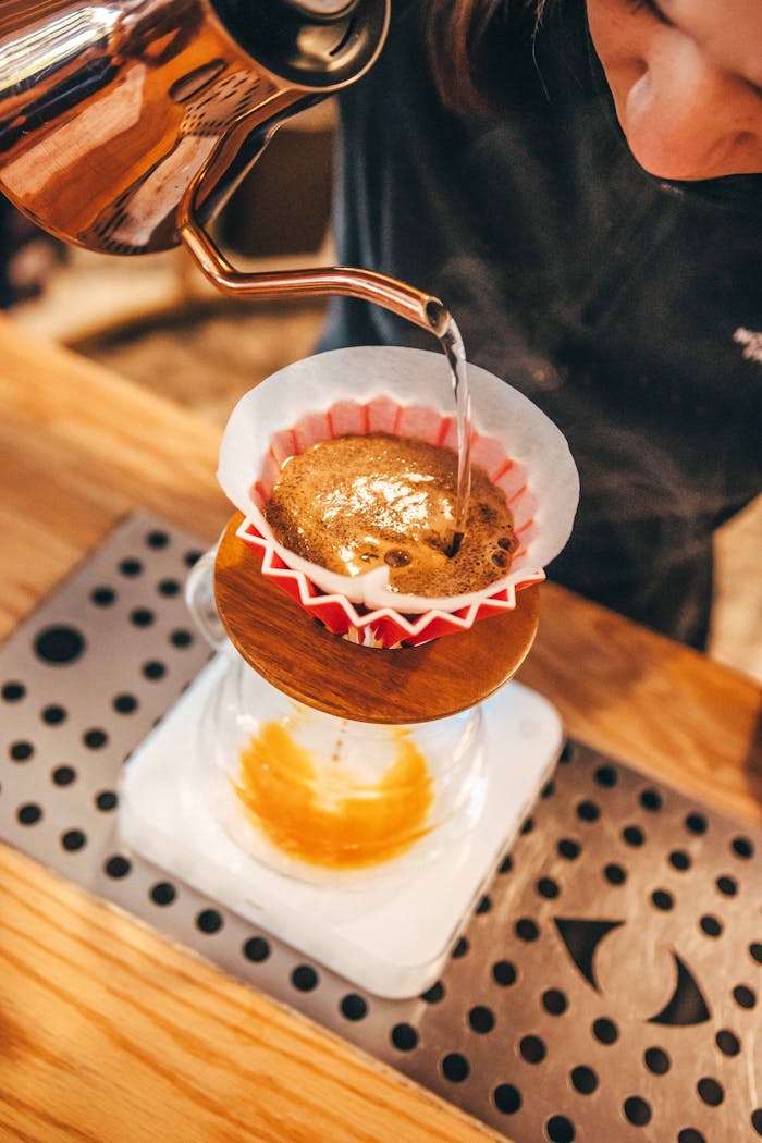 A barista pours hot water over coffee grounds in a filter for a pour-over brew.