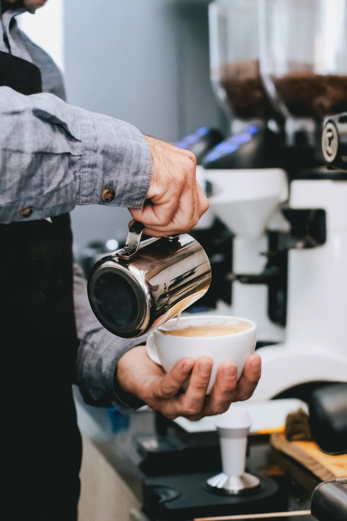 Java Lords Coffee Subscriptions: The Gift That Brews Itself Into Your Life Close-up of barista pouring milk into coffee cup creating latte art in a busy café.